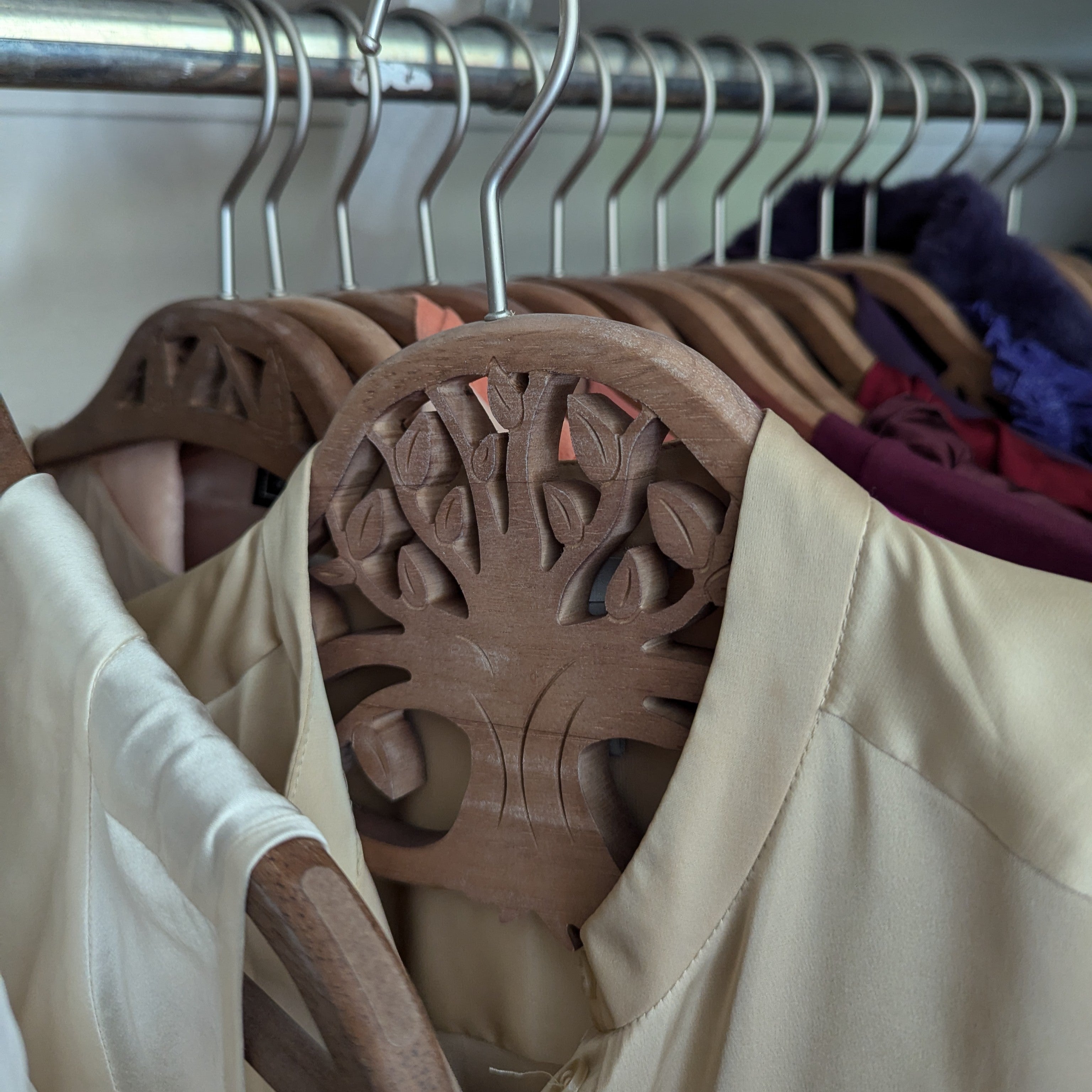 Wooden clothes hangers with decorative cut-out designs holding assorted garments in a closet.