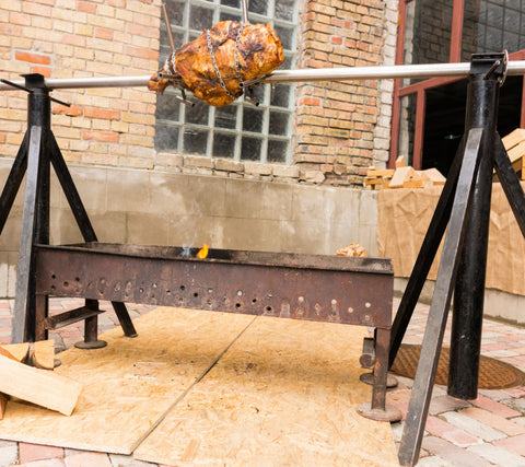 Spit Roaster | Tripod steel framed spit roaster set up in outdoor area cooking chicken