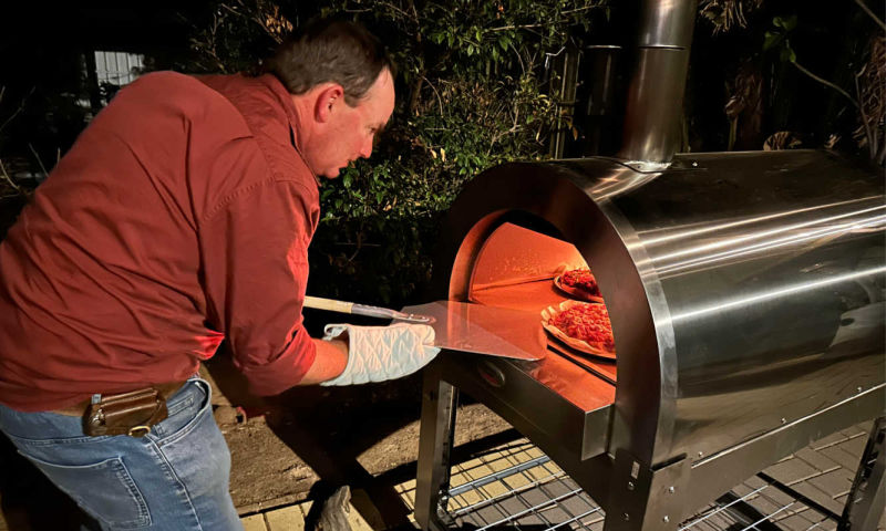 wood fired pizza oven with someone cooking pizzas and about to remove one