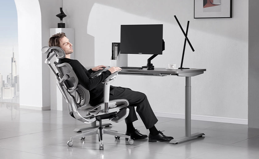 Man reclining comfortably in a Hinomi X1 ergonomic chair at a modern workstation.