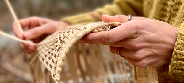 Hands weaving a white oak basket