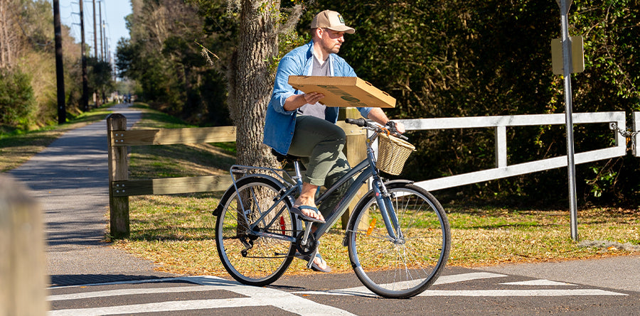 Man wearing Men's Orleans Sandals riding a bike while holding a pizza box