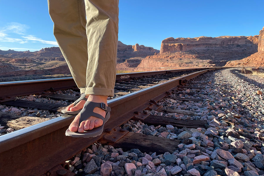 Image of men's feet wearing Tread Labs sandals, balancing on railroad tracks