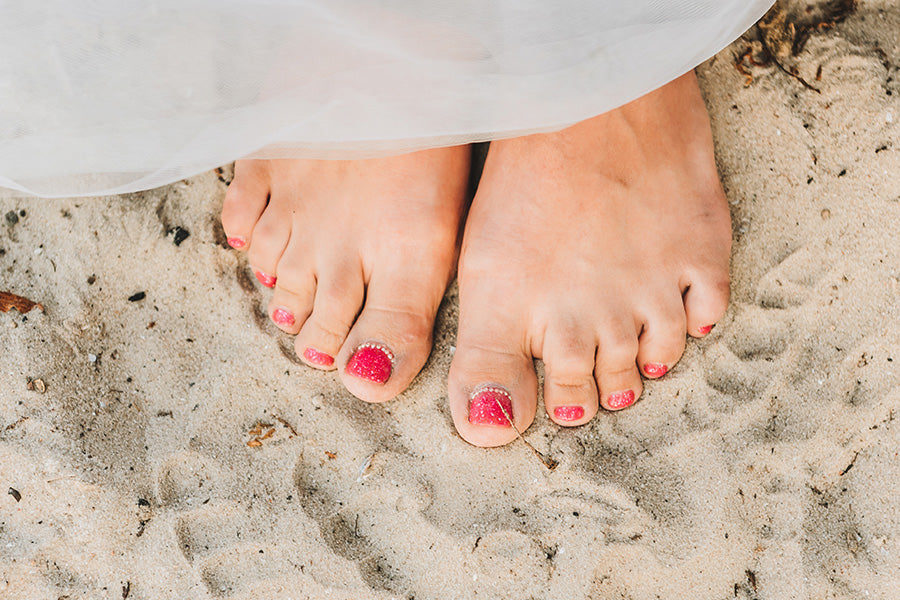 Bare feet in the sand with red toenails.