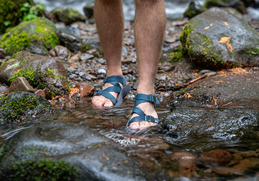 Men's feet in stream wearing Blue Tread Labs Redway Sandals.