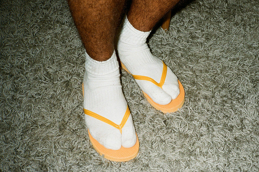 Two feet in white socks and orange plastic flip flops on green shag carpet.