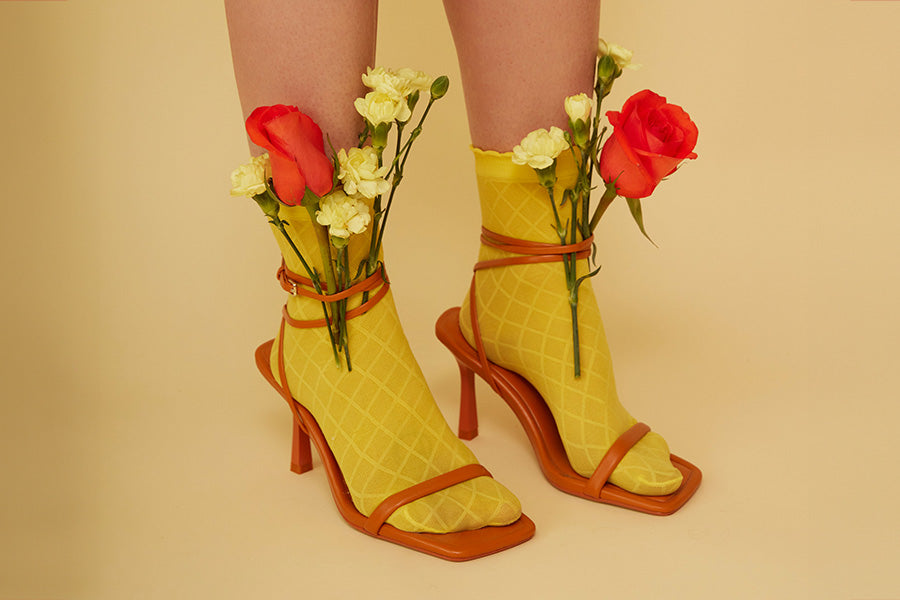Woman's feet in yellow socks and red strap sandals with flowers tucked in the sandal straps.