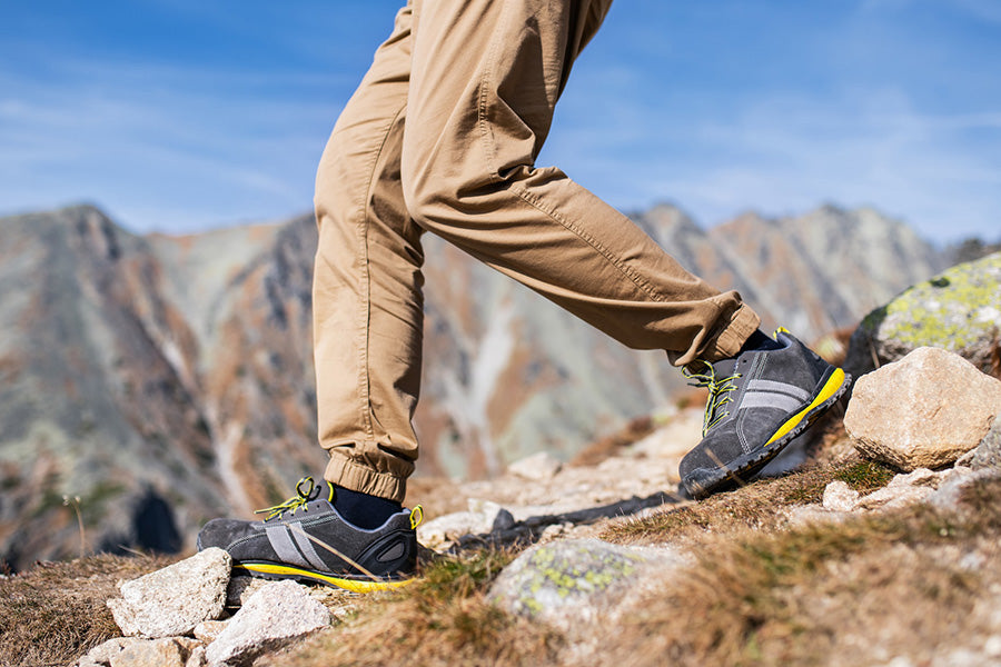 Hikers legs and feet in shoes, descending a ridge with a mountain in the background.