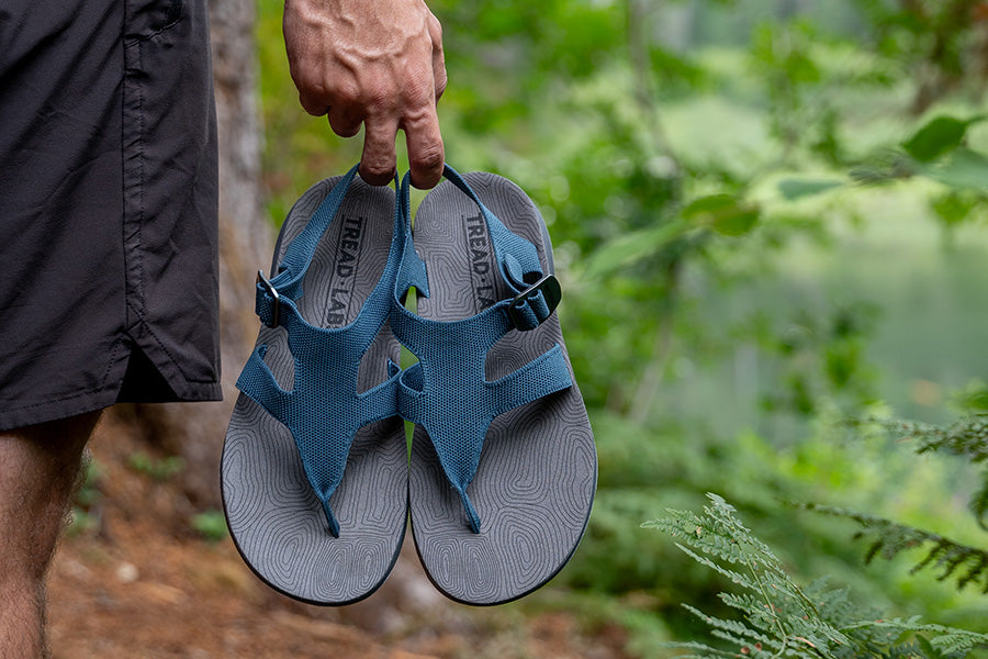 Hand holding a pair of Tread Labs sandals by the heel straps.