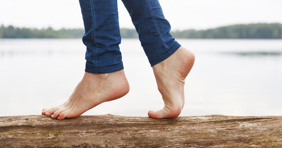 bare feet walking across a log next to a lake