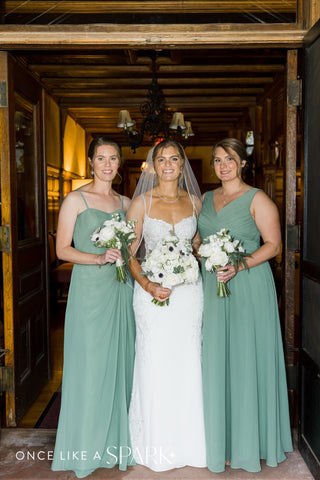 Image of bride with two of her bridesmaids in sage green dresses. All are carrying bouquets with white and green florals.