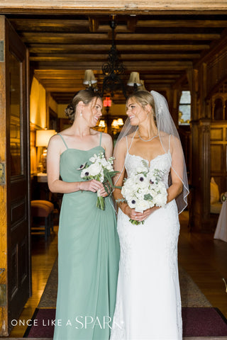 Image of bride and bridesmaid in sage green dress. Both are carryign bouquets with white and green florals.
