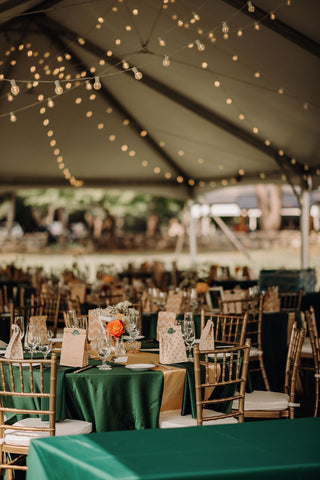 Image of wedding set up at Laurel Springs Farm wedding venue in Massachusetts. Image shows tent with white lights across the top, the tables have a deep green table cloth with pink flower arrangements.