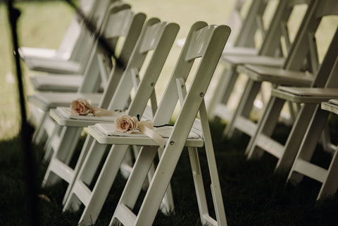 Image of white ceremony chairs with single pale pink roses sitting on a few, in memory of those no longer with us.