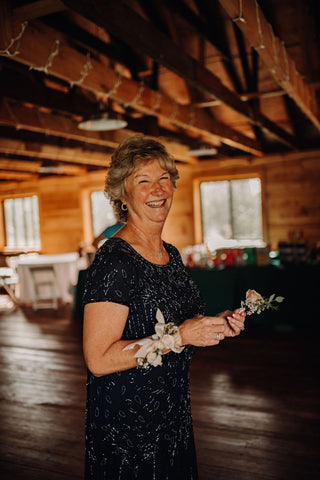 Image of mother of groom smiling on wedding day. She is wearing a beautiful floral corsage.