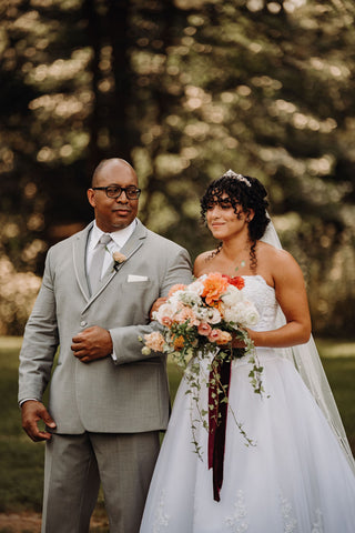 Bride and her father walking down the aisle at couple's wedding at Laurel Spring Farms in Massachusetts. The father of the bride is in a pale gray suit. The bride is carrying a bouquet in shareds of pink.