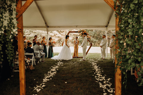 Image zoomed out of wedding ceremony. Camera took photo through the chuppah looking fown the rose lined aisle with bride and groom during ceremony with hexagonal arch with pink floral design.