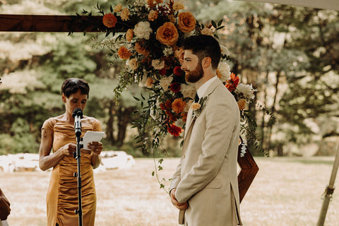 Image of groom and officiant during the wedding ceremony. The backdrop is a stunning floral installation on a heagonal arch. The arch is designed with flowers in shades of pink.
