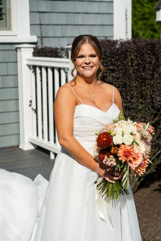 Image of bride on her wedding day. She is in her wedding gown, holding a muted  early fall bridal bouquet.