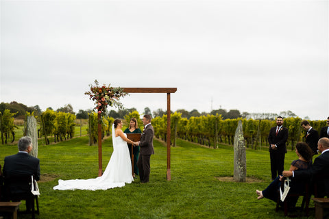 Image of bride and grooms first kiss in front of floral installation wedding arbor overlooking Newport Vineyards.