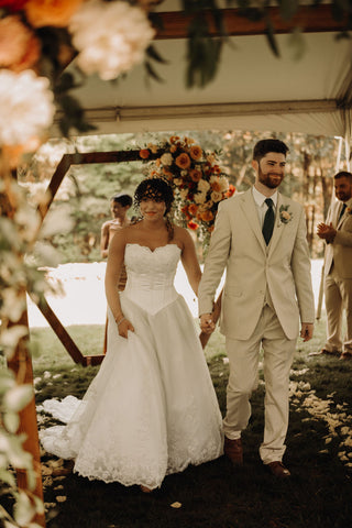 Image of bride and groom walking down the aisle after ceremony. You can see their happiness and the flower installation on their wedding arch in the background.