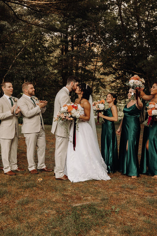 Image of groupwedding photo of wedding party at Laurel Spring Farms wedding venue in Massachusetts. The groom and grommsmen arre wearing khaki colored suits and the brdiesmaids are wearing emerald green long dresses. They bouquets are in shades of pink flowers.