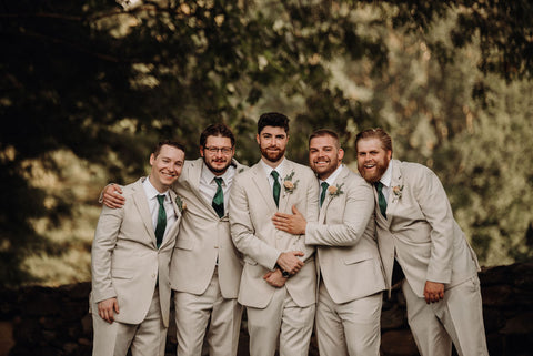 Image of groomsmen and groom. They are all wearing sand colored suits with green ties and pale pink boutonnieres.