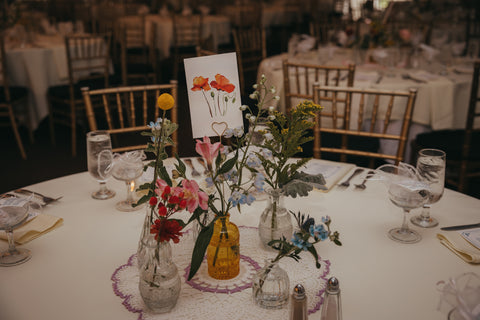 wedding centerpiece with colorful bud vases. Flowers include Peonies, gerberas, snapdragons, poppies, roses, ranunculus, chamomile, delphinium, craspedia, alstroemeria, hypericum, solidago, roses, stock, larkspur, wildflowers.