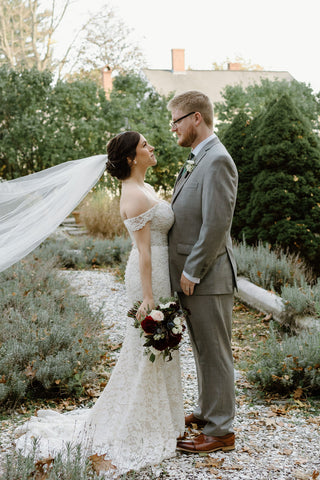 Bride and groom, fall wedding. Bride is holding a beautiful vibrant bridal bouquet with deep red dahlias, creamy white roses, pale pink roses, anemones and greenery