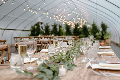 Herb Lyceum greenhouse, as wedding venue in Groton, MA/New England set up for a wedding reception. Long tables adorned with greenery. Trees in the background of the green house.