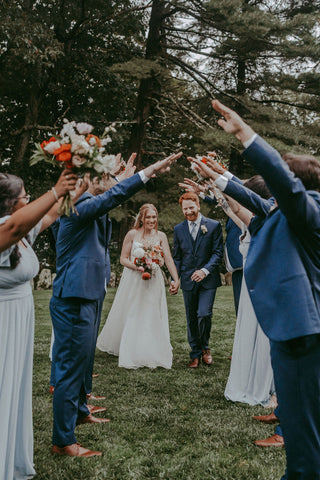 Image of bride and groom walking through an aisle created by wedding party with their arms in air over them.