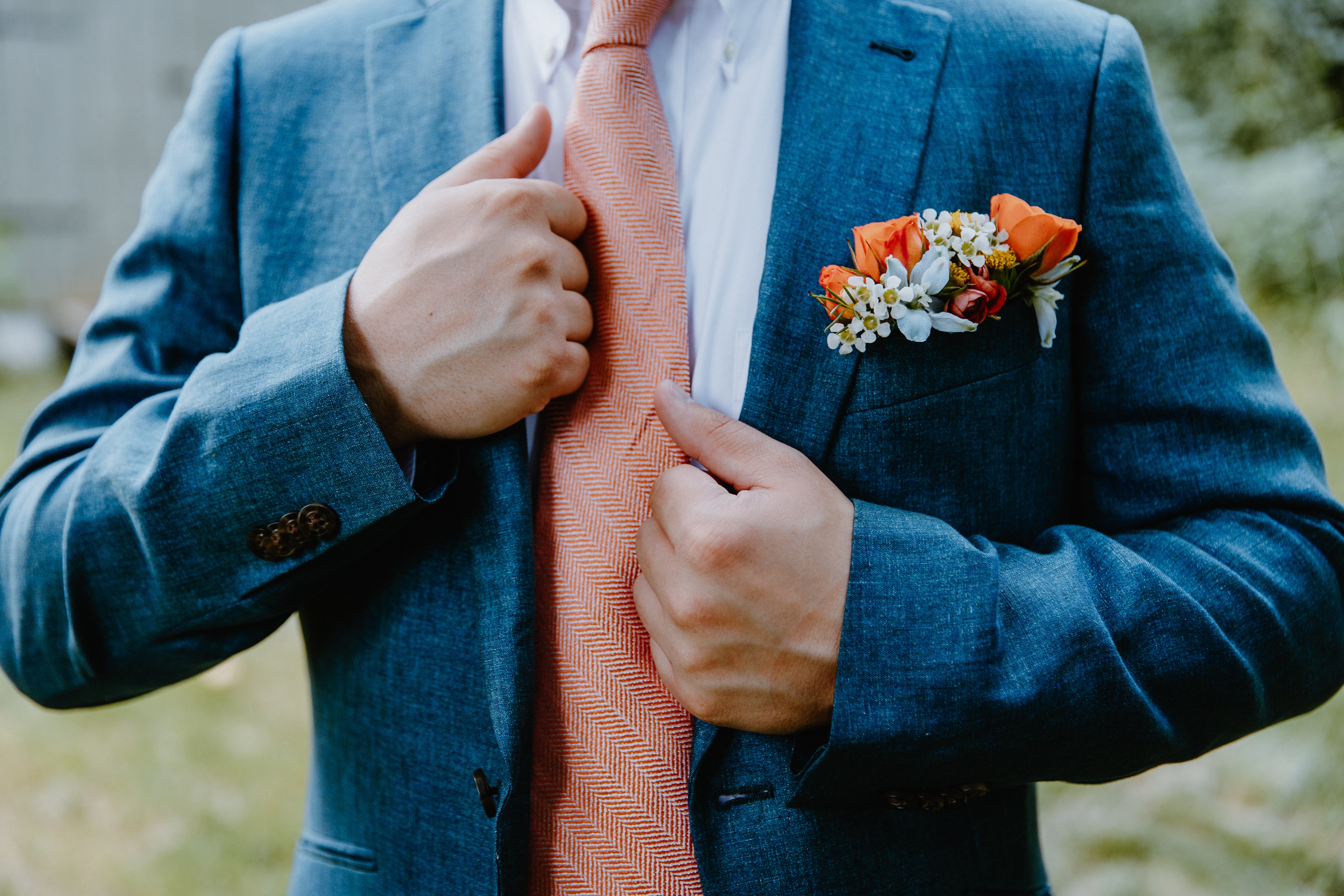 Image of a pocket swuare floral in a suit jacket. the image is zoomed in on the pocket square floral. It has orange and bright flowers, against a blue suit.