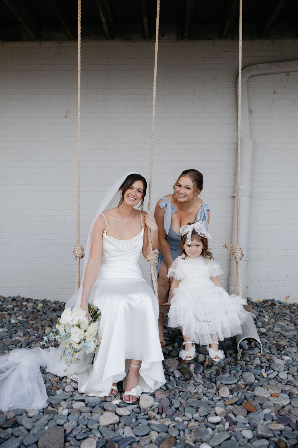 Image of a bride, bridesmaid and flower girl on the swing at the Oceanview of Nahant.