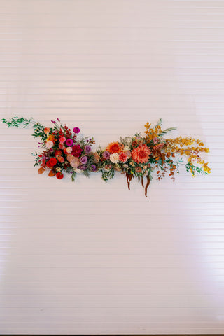 Image of a muted fall color palette wedding statement floral installation in pinks, oranges, purples, yellow and white.