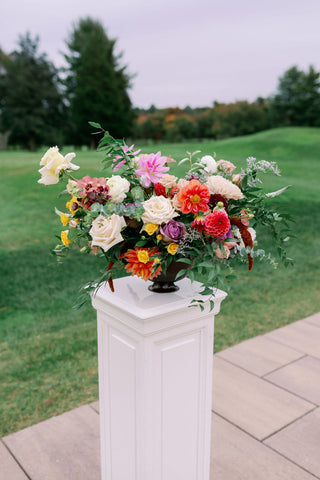 Image of fall wedding ceremony flower arrangements on white pedestal. The flowers include unique flowers in muted fall colors.