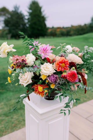 Image of muted fall ceremony flower arrangements on pedestals. The flowers include pinks, purples, oranges, yellows and whites.