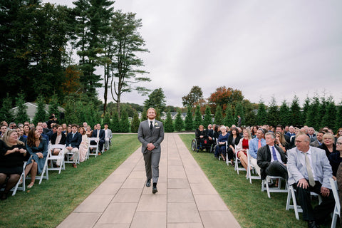 Image of groomsman walking down the aisle at the outdoor wedding ceremony space at the Cape Club of Sharon.