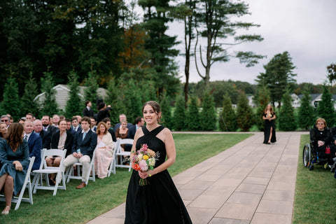 Image of bridesmaid walking down the aisle at the utdoor ceremony space at the Cape Club of Sharon.