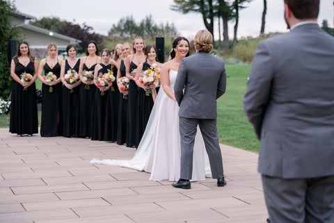 Image of bride and groom during weddingg ceremony at the outdoor space at the Cape Club of Sharon.  Image shows an angle where you see the line of bridesmaids behind the bride.