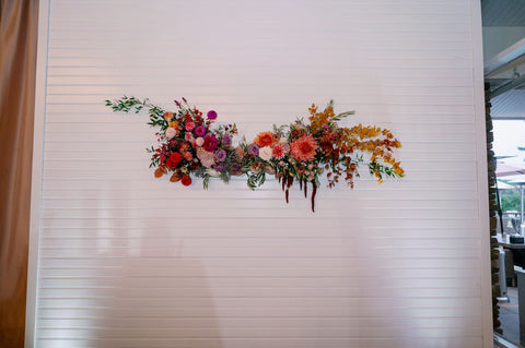 Image of muted fall color floral installation on wall at the Cape Club of Sharon. The installation includes flowers in shades of pink, purple, orange, yellow and white.