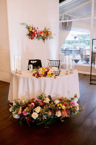 Image of sweetheart table set up at the Cape Club of Sharon. There is a muted fall colored floral installation on the wall over the table, flowers on the table and below.