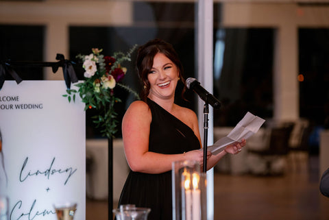Image of maid of honor giving her speech. She is wearing a black dress and smiling as she speaks.