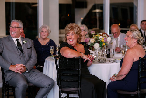 Image of wedding fuests laughing as maid of honor gives her speech.