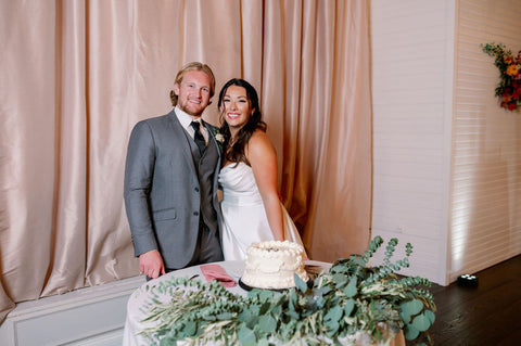 Image of bride and groom in front of their wedding cake that says "Just Married".