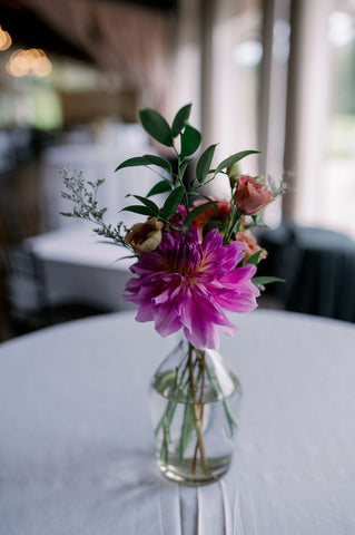 Image of a bud vase floral design for a wedding reception in a purple fal lcolor, dahlia featured.