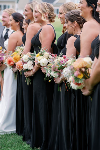 Zoomed in image of bridesmaids from a unique angle that highlgihts the brdiesmaids bouquets in muted fall colors including: dahlias, marigolds, sedum, celosia, ranunculus, lisianthus, mums, leucadendron, asclepia, eucalyptus, and amaranthus.