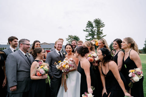 Image of wedding party. Bridesmaids are dressed in long black dresses, groomsmen are in gray suits.