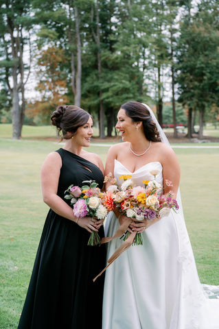 Image of bride and maid of honor. Both are holding bouquets with flowers of muted fall colors.