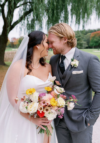 Image of bride and groom with foreheads touching. A romatic photo with the couples looking into each others eyes underneath a tree. The bride is holding a lush bridal bouquet in a muted fall color palette.