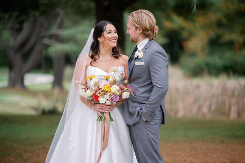 Image of bride and groom during the couple portraits at the Cape Club of Sharon, a Massachuetts wedding venue. They are lovingly looking into each others eyes. The bride is holding a lush bouquet in a muted fall color palette with dahlias, marigolds, sedum, celosia, ranunculus, lisianthus, mums, leucadendron, asclepia, eucalyptus, and amaranthus.